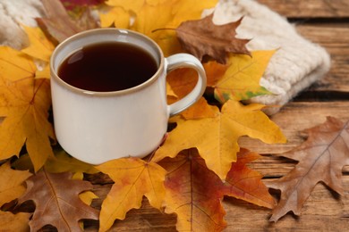 Cup of hot tea and autumn leaves on wooden table, space for text