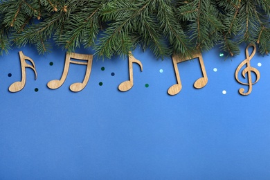 Photo of Fir tree branches with wooden music notes and space for text on blue background, flat lay. Christmas celebration