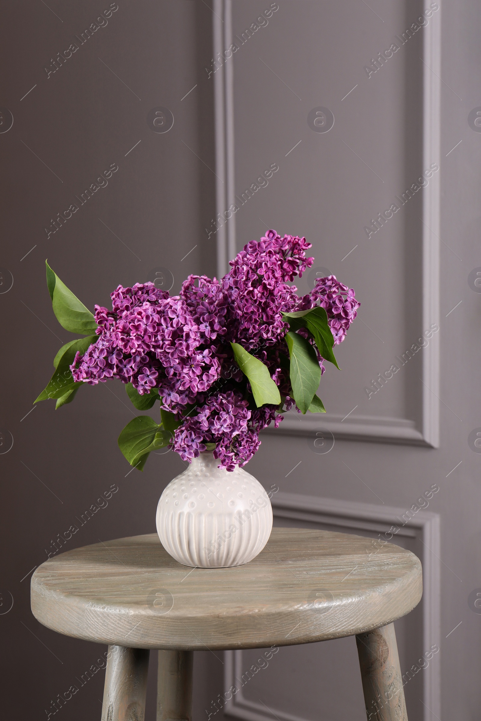 Photo of Beautiful lilac flowers in vase on wooden table near light wall