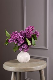 Beautiful lilac flowers in vase on wooden table near light wall