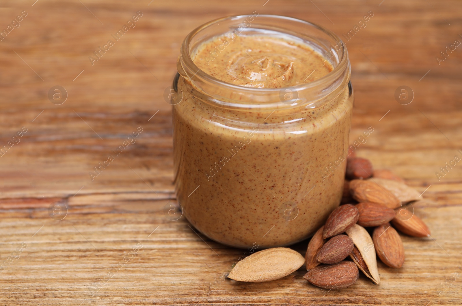 Photo of Tasty nut paste in jar and almonds on wooden table, closeup. Space for text