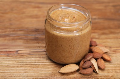 Tasty nut paste in jar and almonds on wooden table, closeup. Space for text