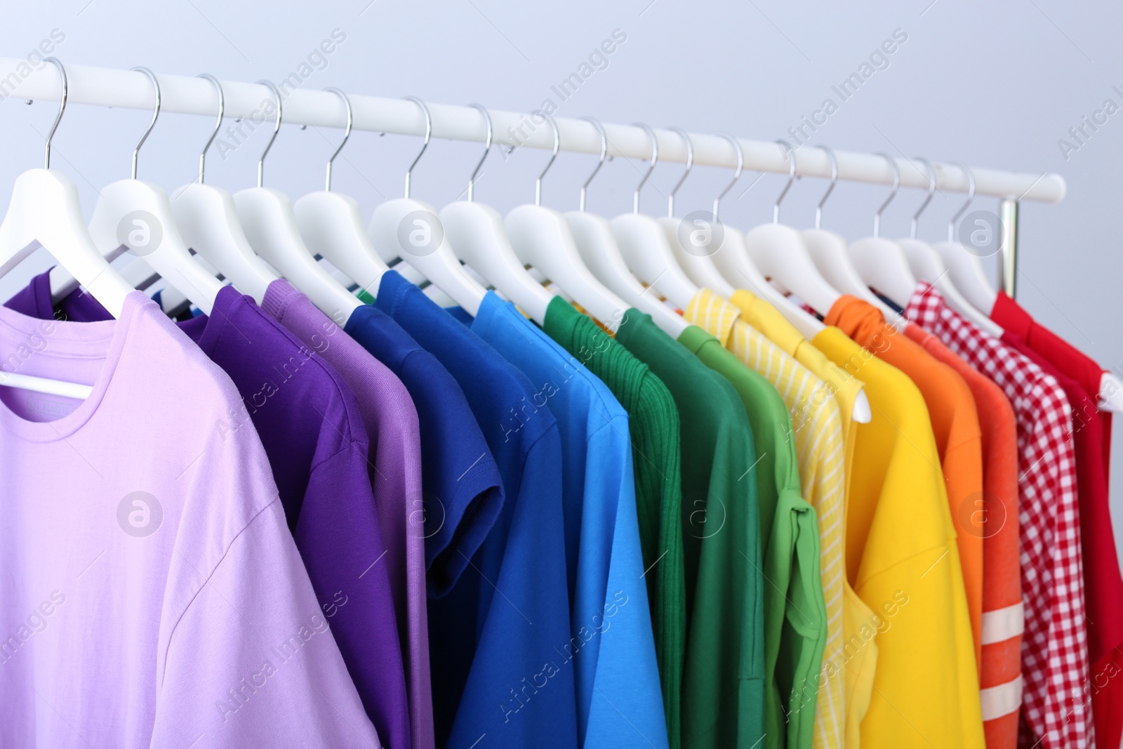 Photo of Rack with rainbow clothes on light background