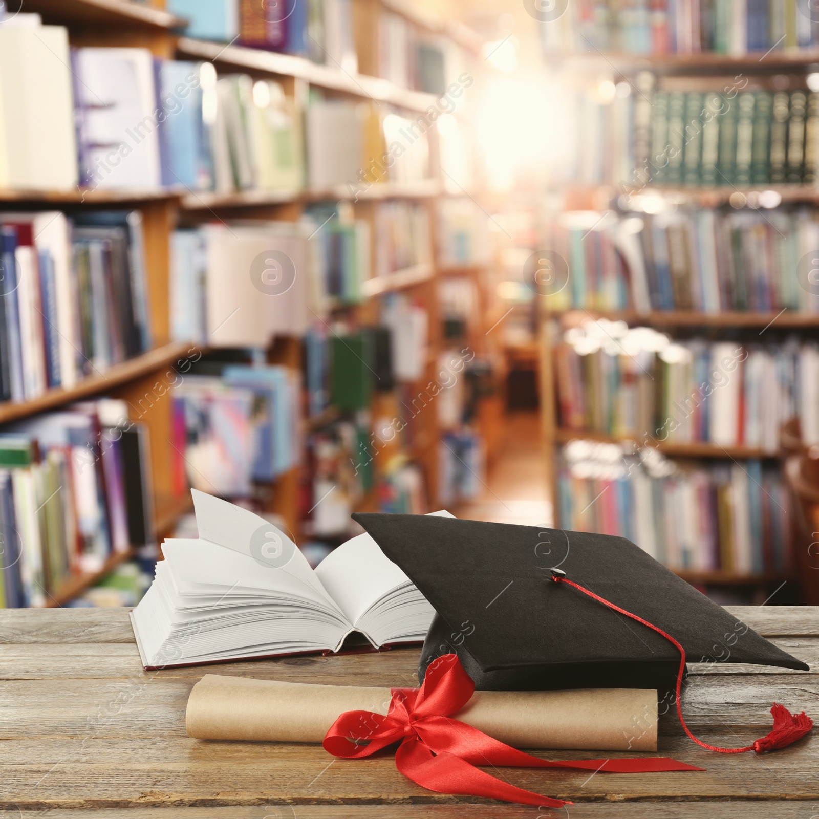 Image of Graduation hat, book and diploma on wooden table in library