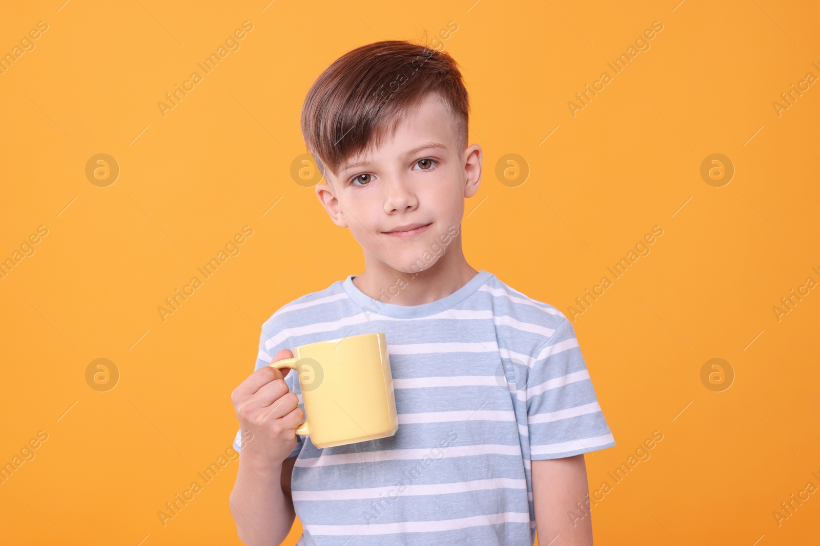 Photo of Cute boy with yellow ceramic mug on orange background