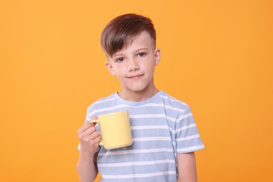 Photo of Cute boy with yellow ceramic mug on orange background