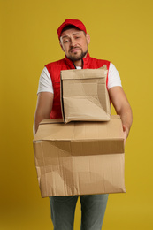 Photo of Emotional courier with damaged cardboard boxes on yellow background. Poor quality delivery service
