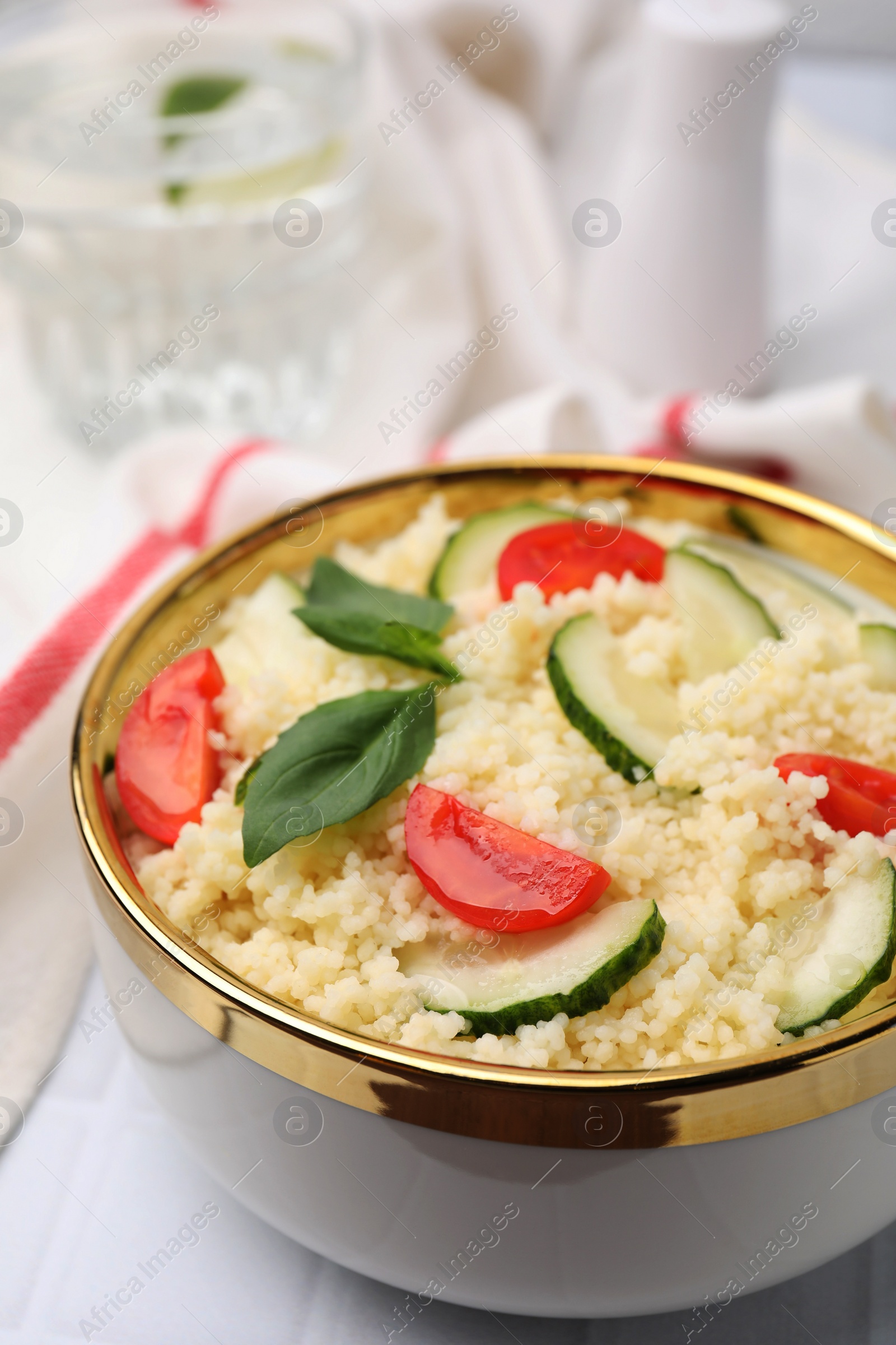 Photo of Tasty couscous with tomatoes, cucumber and basil on white tiled table, closeup