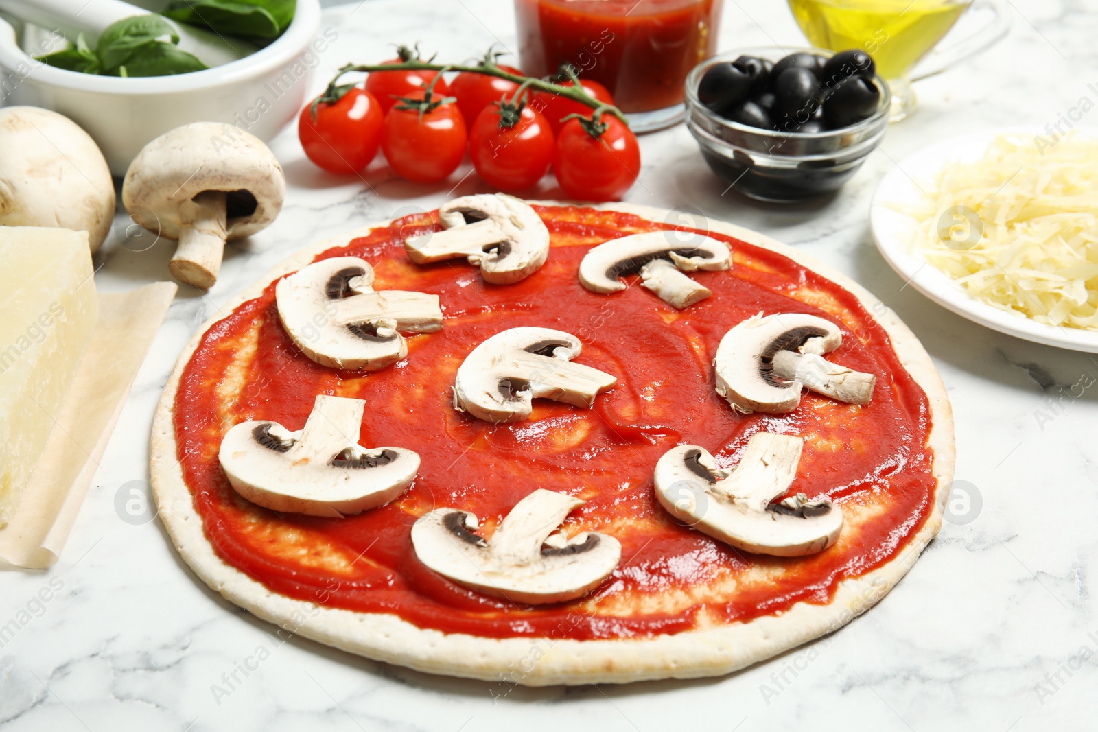 Photo of Pizza crust with tomato sauce, mushrooms and ingredients on marble table