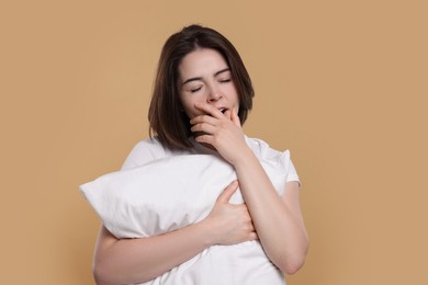 Photo of Sleepy young woman with pillow yawning on beige background. Insomnia problem