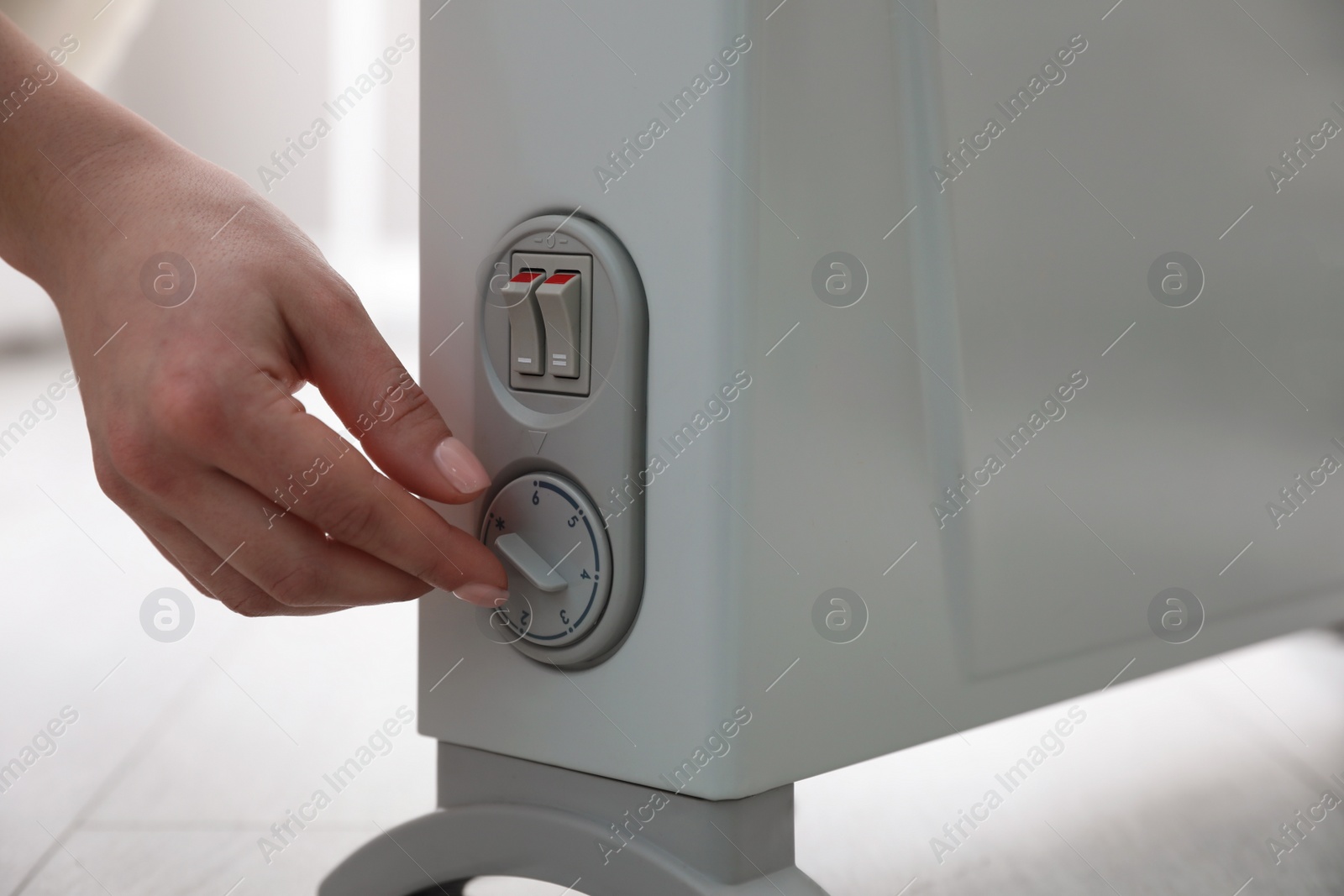 Photo of Woman turning on electric heater at home, closeup