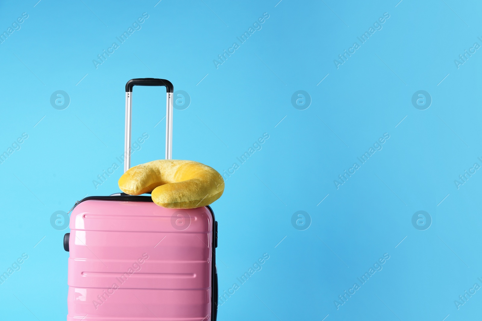 Photo of Pink suitcase and travel pillow on light blue background, space for text