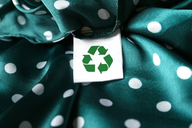 Image of Clothing label with recycling symbol on green garment, closeup