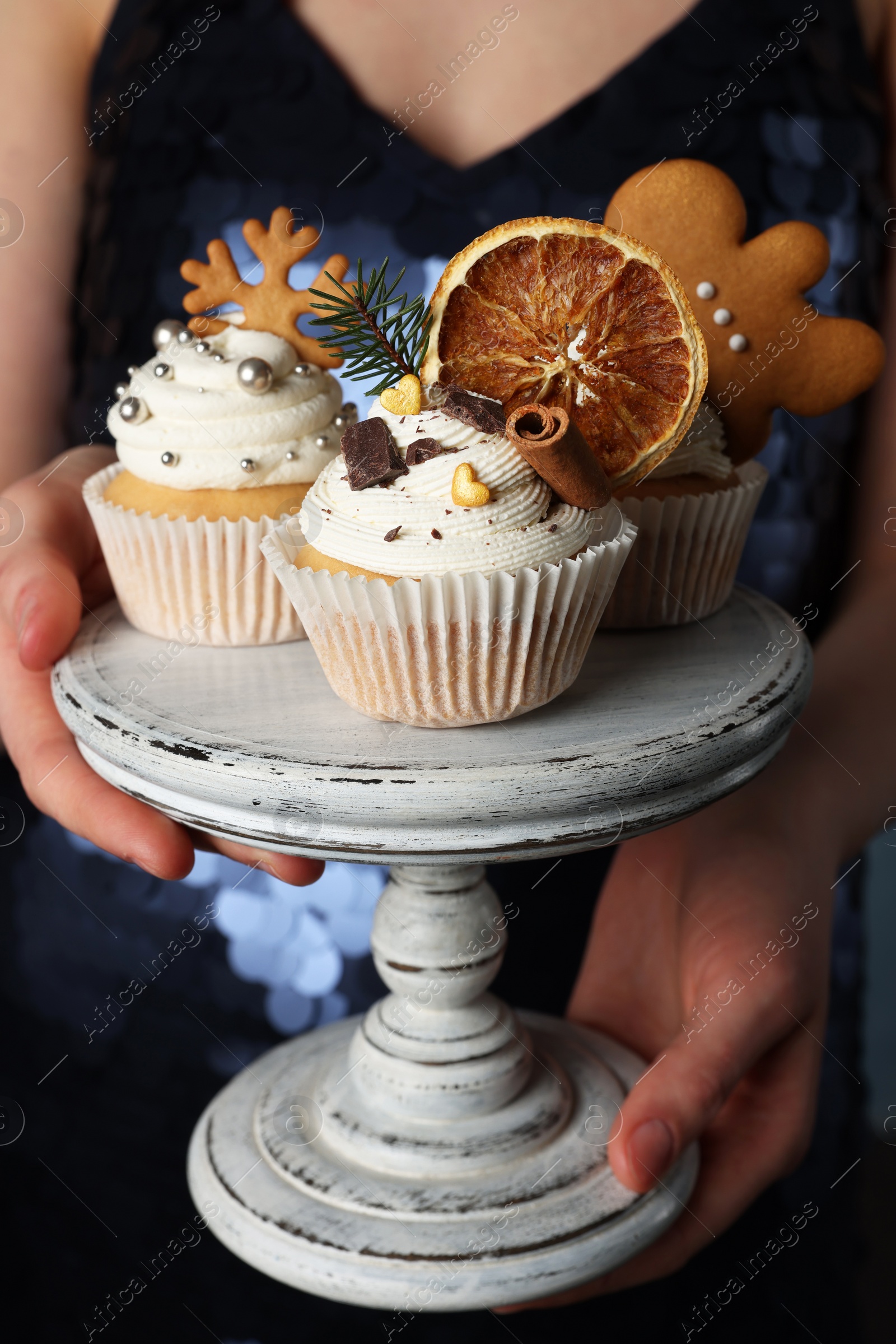 Photo of Woman holding dessert stand with tasty Christmas cupcakes, closeup