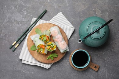 Photo of Tasty spring rolls served on grey textured table, flat lay