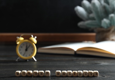 Cubes with phrase Winter Holidays on black wooden table in classroom. Space for text