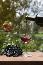 Pouring red wine from bottle into glass at wooden table outdoors, closeup