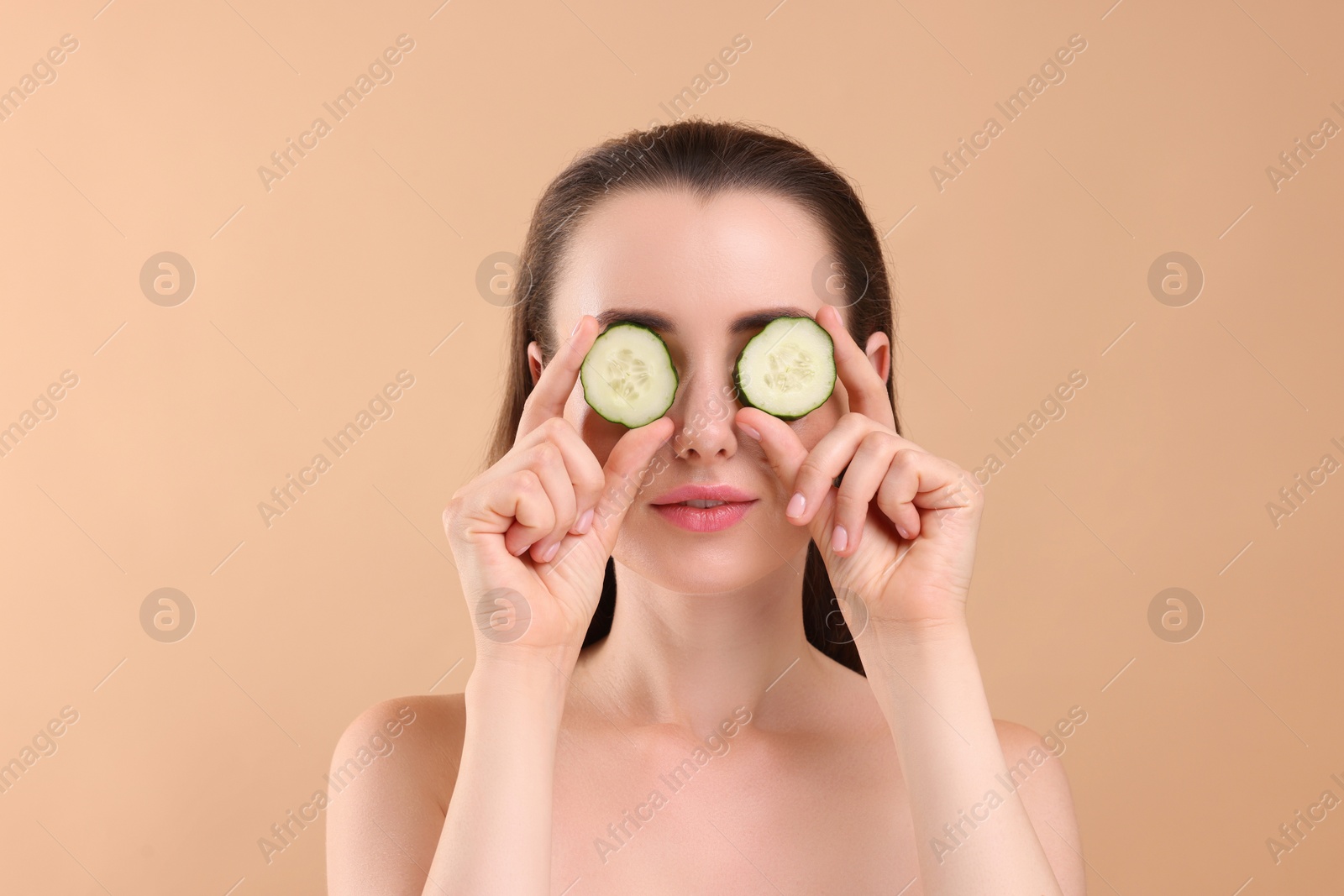 Photo of Beautiful woman covering eyes with piece of cucumber on beige background