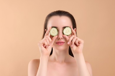 Beautiful woman covering eyes with piece of cucumber on beige background