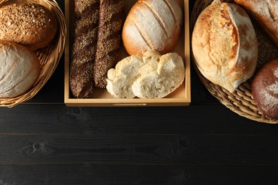 Photo of Wicker baskets with different types of fresh bread on black wooden table, flat lay. Space for text