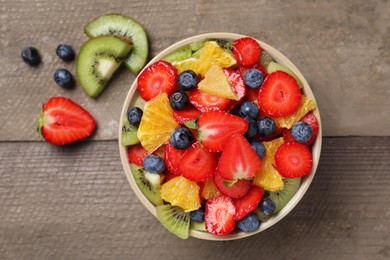 Delicious fresh fruit salad in bowl and ingredients on wooden table, flat lay