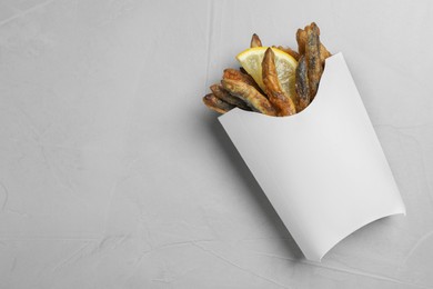 Paper bag with delicious fried anchovies and lemon slice on light table, top view. Space for text