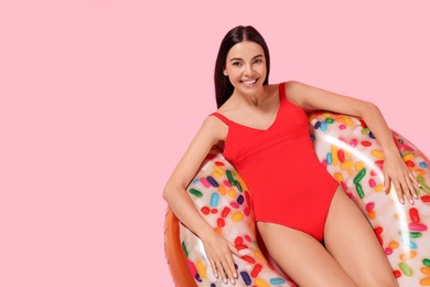 Photo of Young woman in stylish swimsuit on inflatable ring against pink background, above view. Space for text