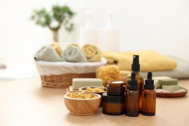 Photo of Bottles of essential oils, dry flowers and jars with cream on light wooden table. Spa therapy