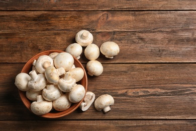 Bowl of fresh champignon mushrooms on wooden background, top view with space for text