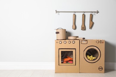 Photo of Cardboard kitchen and washing machine near white wall indoors. Space for text