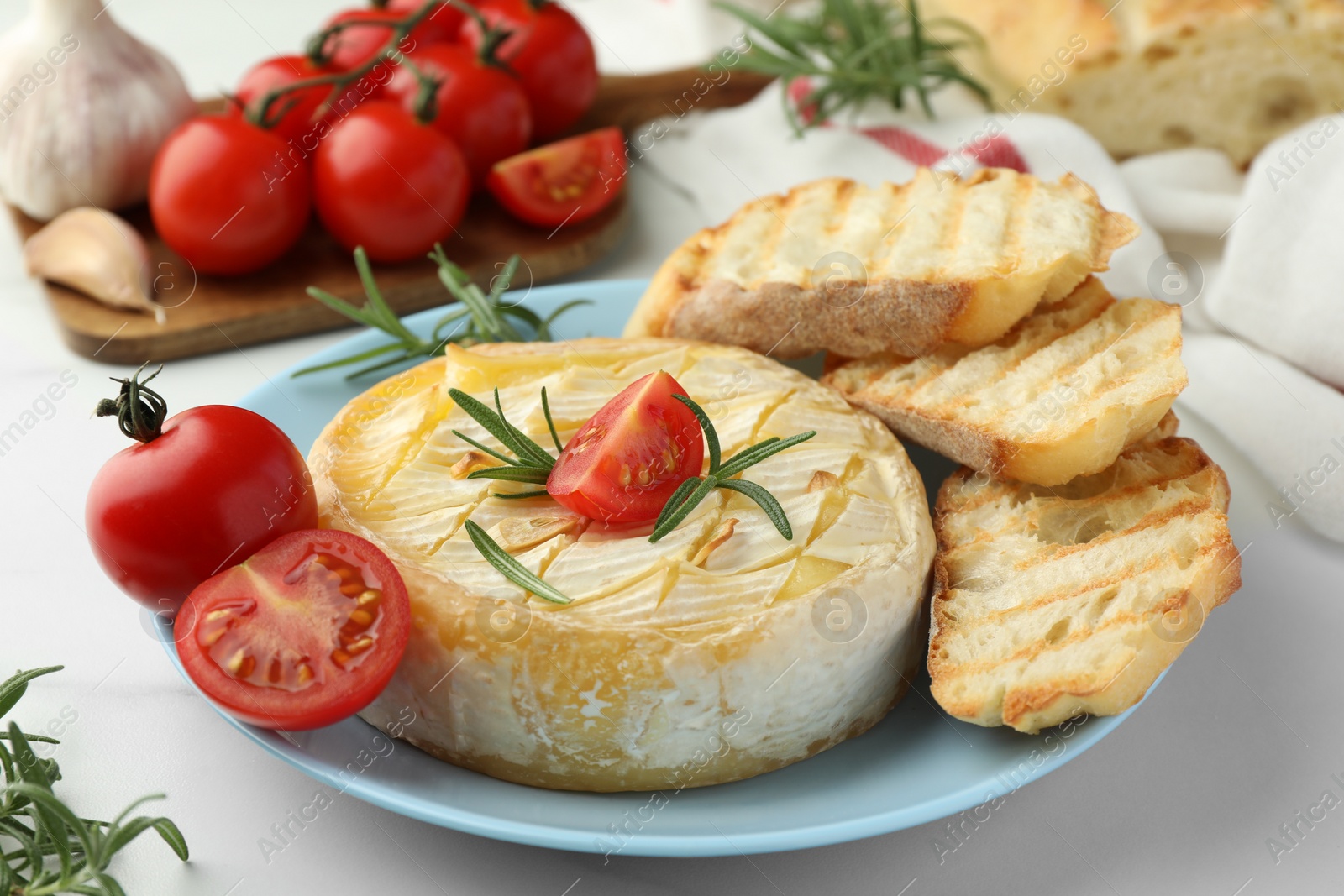 Photo of Tasty baked brie cheese with rosemary, cherry tomatoes and bread on white table, closeup