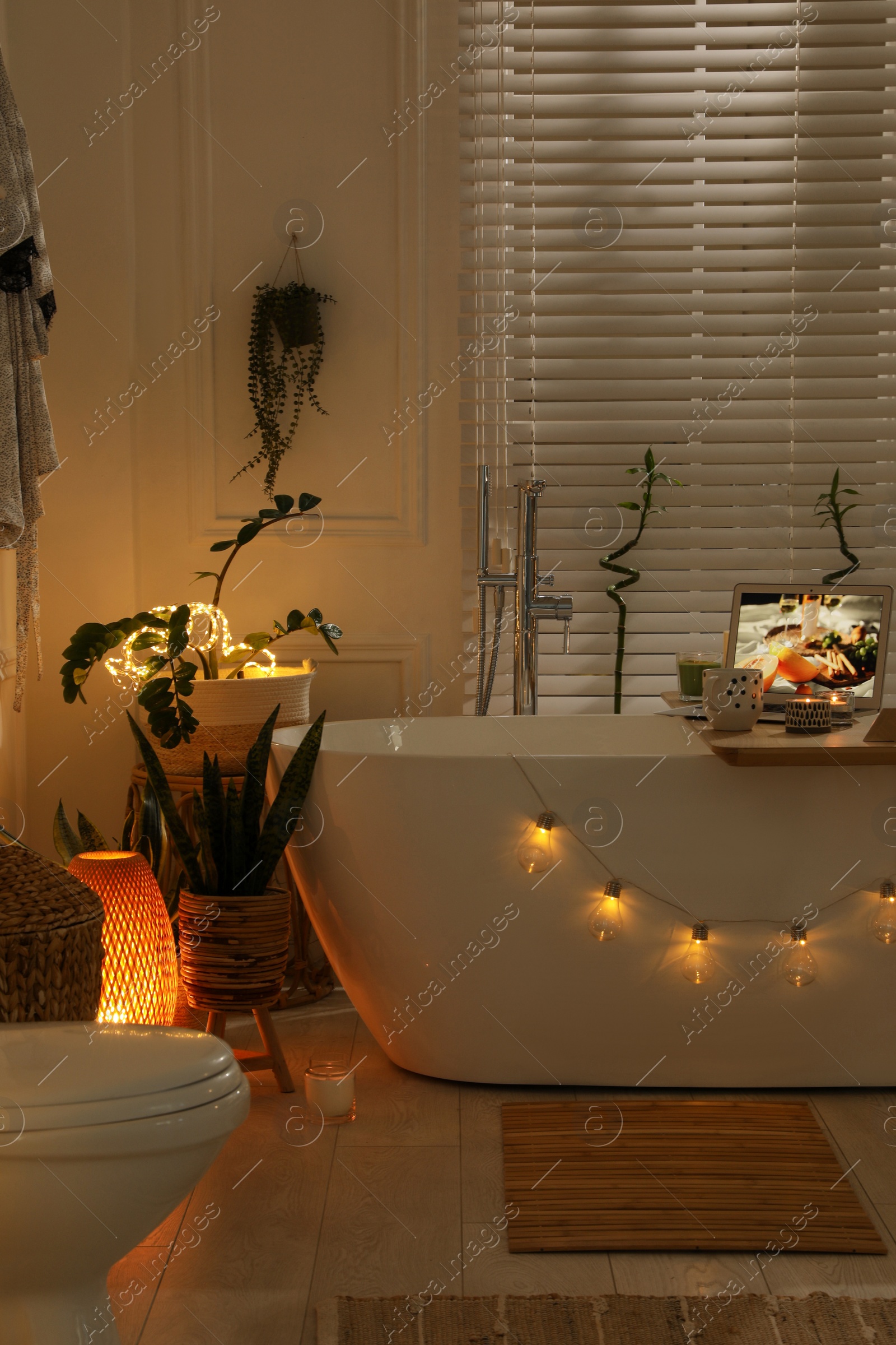 Photo of Stylish bathroom interior with green houseplants and string lights. Idea for design