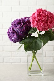 Photo of Vase with beautiful hortensia flowers on light table near white brick wall