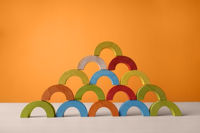Photo of Colorful wooden pieces of educational toy on light table against orange wall. Motor skills development