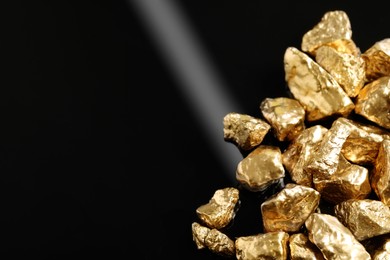 Pile of shiny gold nuggets on black background, closeup. Space for text