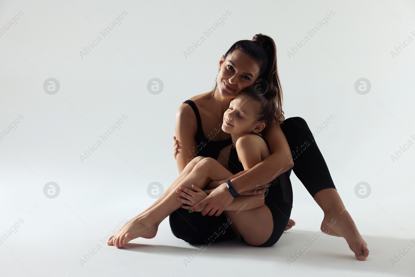 Photo of Little gymnast and her coach sitting on white background