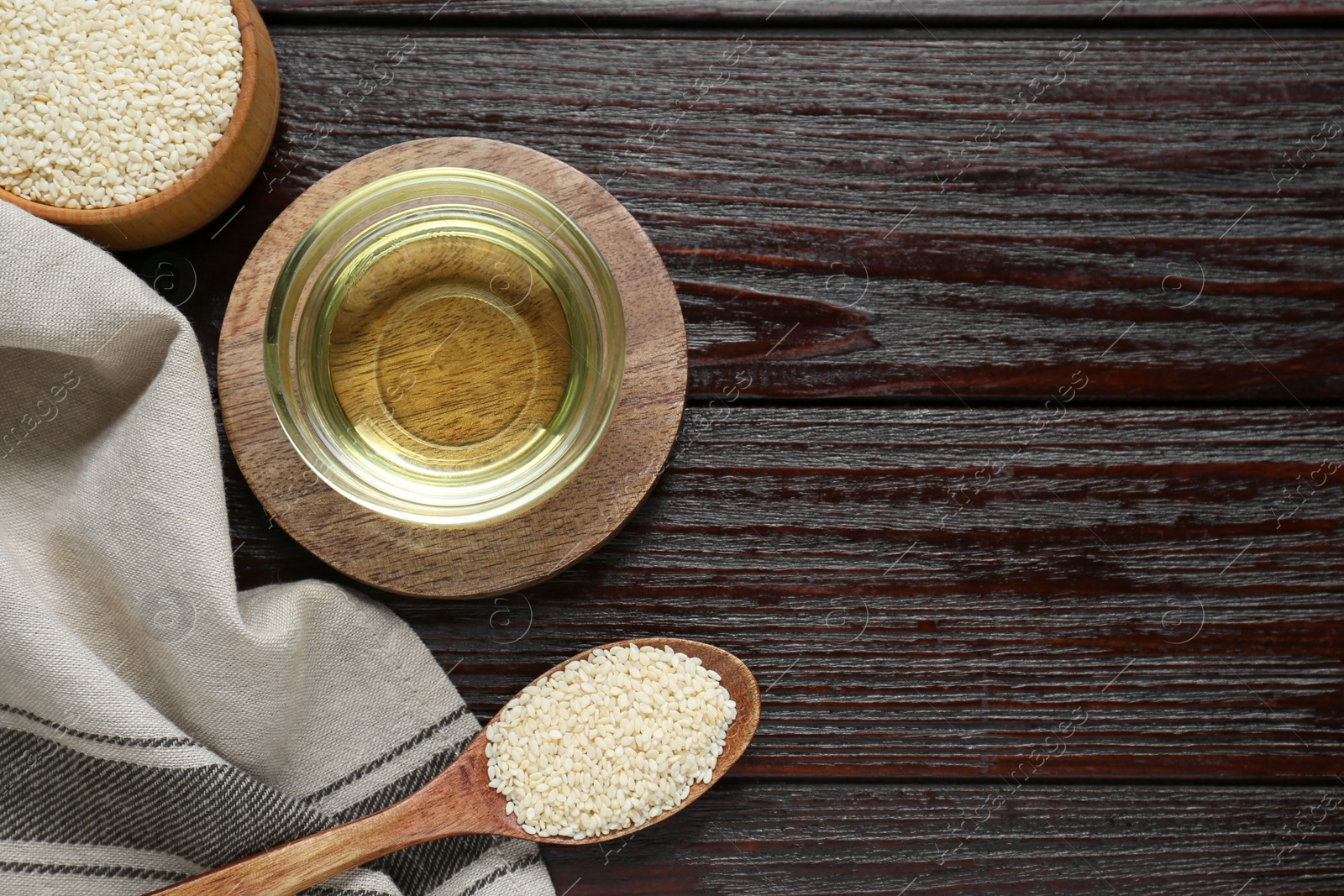 Photo of Fresh sesame oil in glass bowl and seeds on dark wooden table, flat lay. Space for text