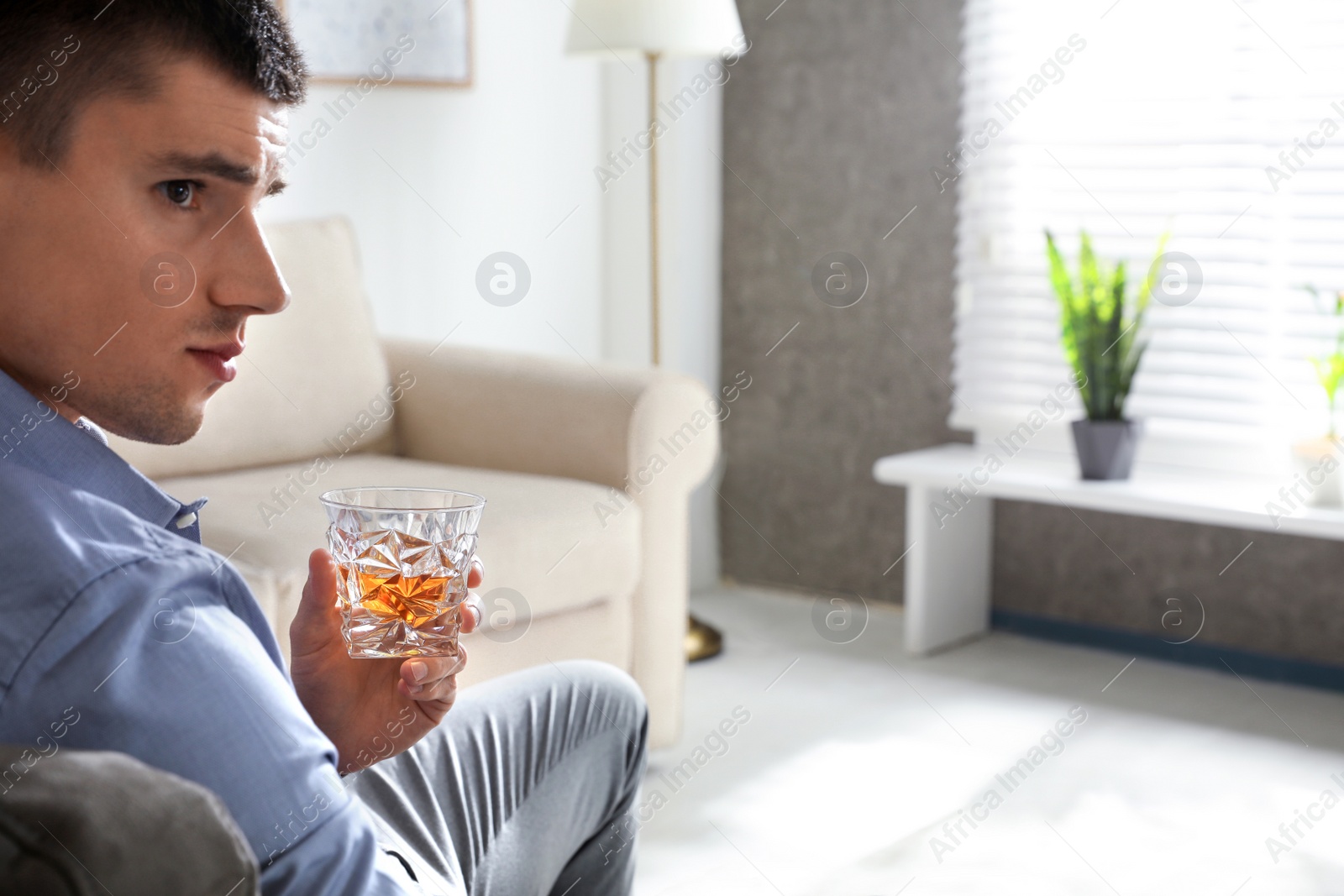 Photo of Young man with glass of whiskey at home. Space for text