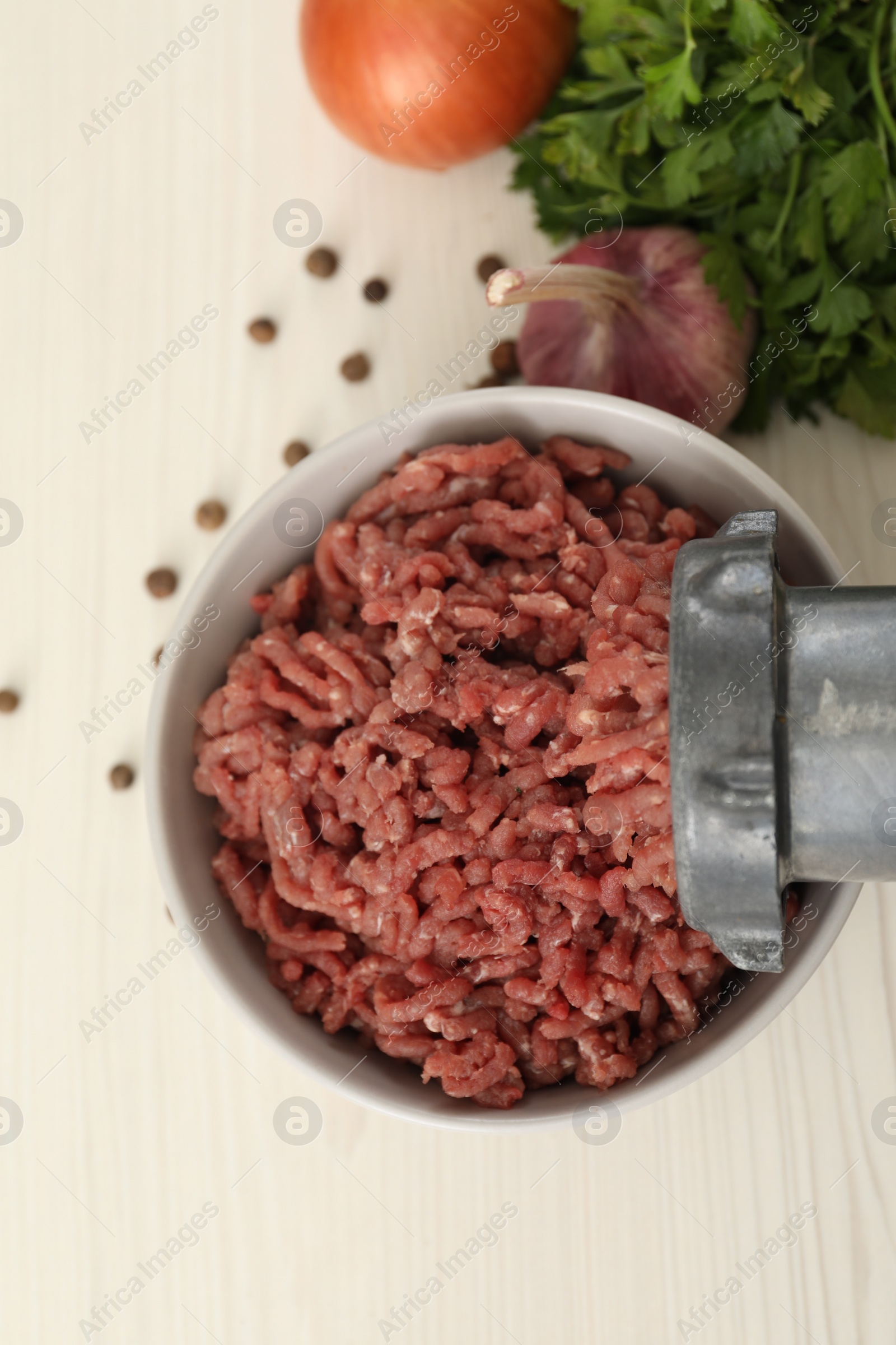 Photo of Mincing beef with meat grinder. Parsley, garlic and peppercorns on white wooden table, flat lay