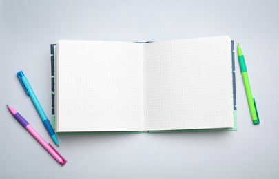 Stylish open notebook and pens on light grey background, flat lay