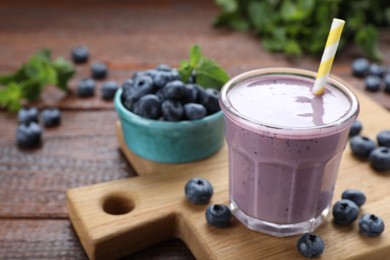 Glass of blueberry smoothie with fresh berries on wooden table, closeup. Space for text