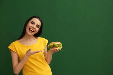 Young woman with tasty burger on color background. Space for text