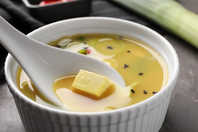 Photo of Eating delicious miso soup with tofu from bowl on table, closeup