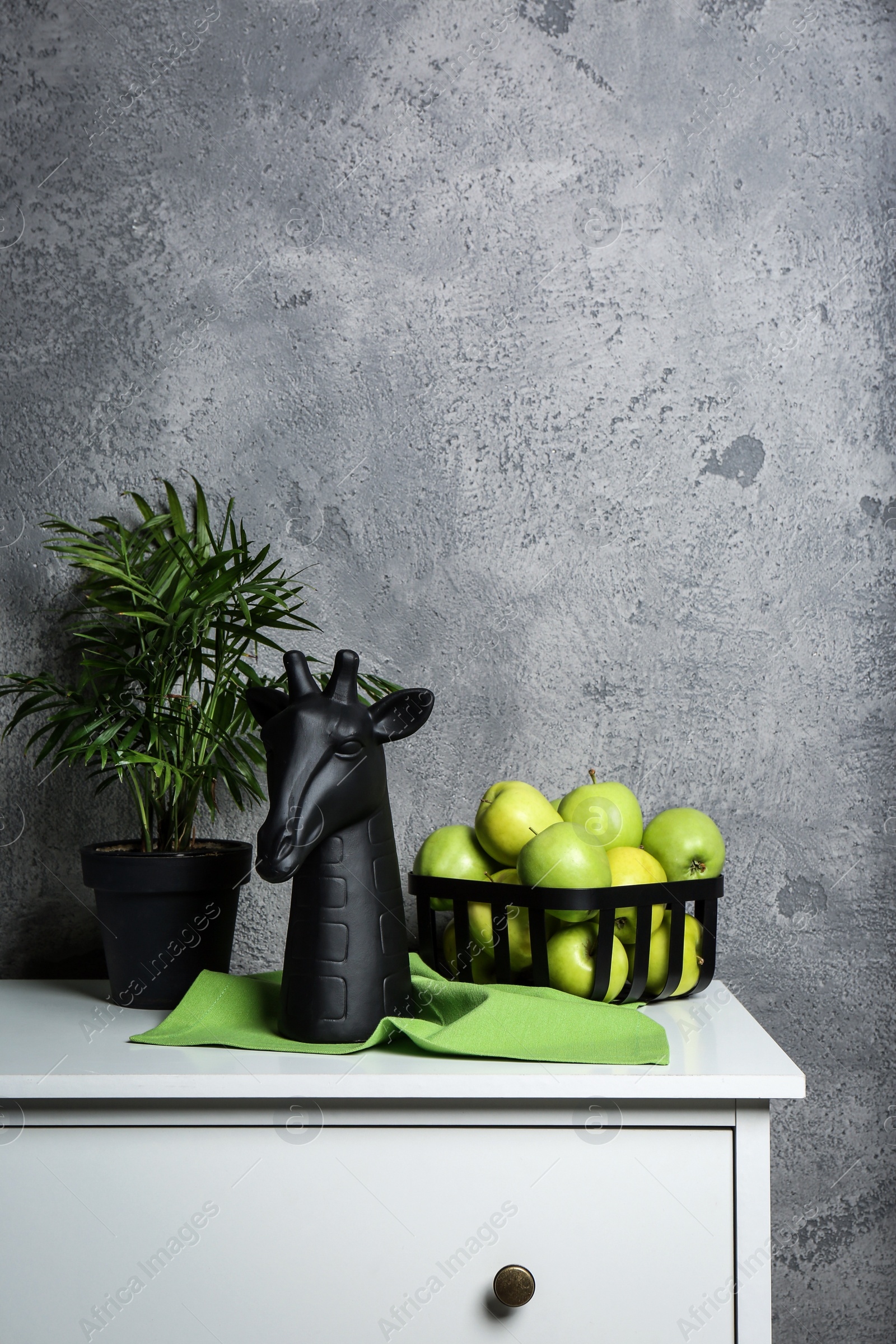 Photo of Stylish decor, basket with apples and houseplant on chest of drawers near grey wall indoors, space for text. Interior design