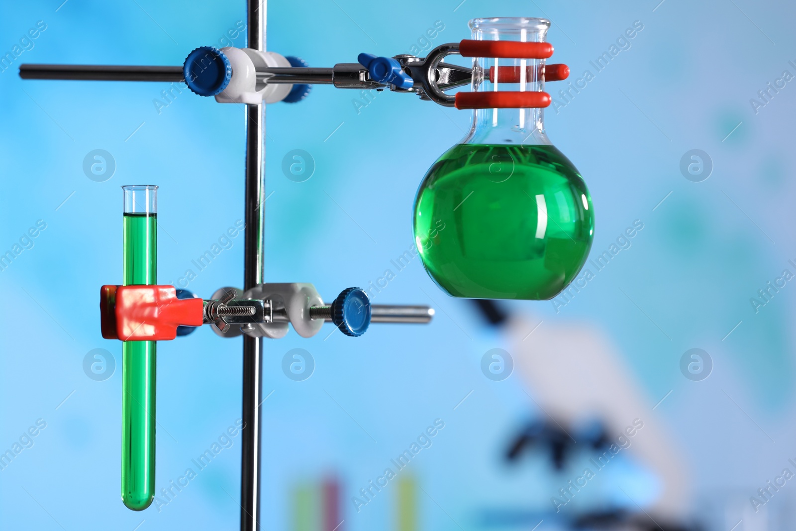 Photo of Laboratory glassware with green liquid on retort stand indoors, closeup