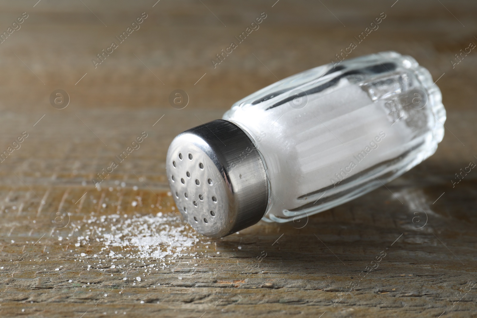 Photo of Organic salt in glass shaker on wooden table, closeup