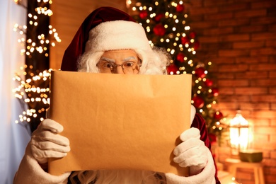 Photo of Santa Claus reading wish list in festively decorated room