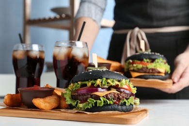 Woman with black burger, fries and drinks served on table in cafe