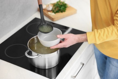 Man pouring delicious soup into bowl in kitchen, closeup