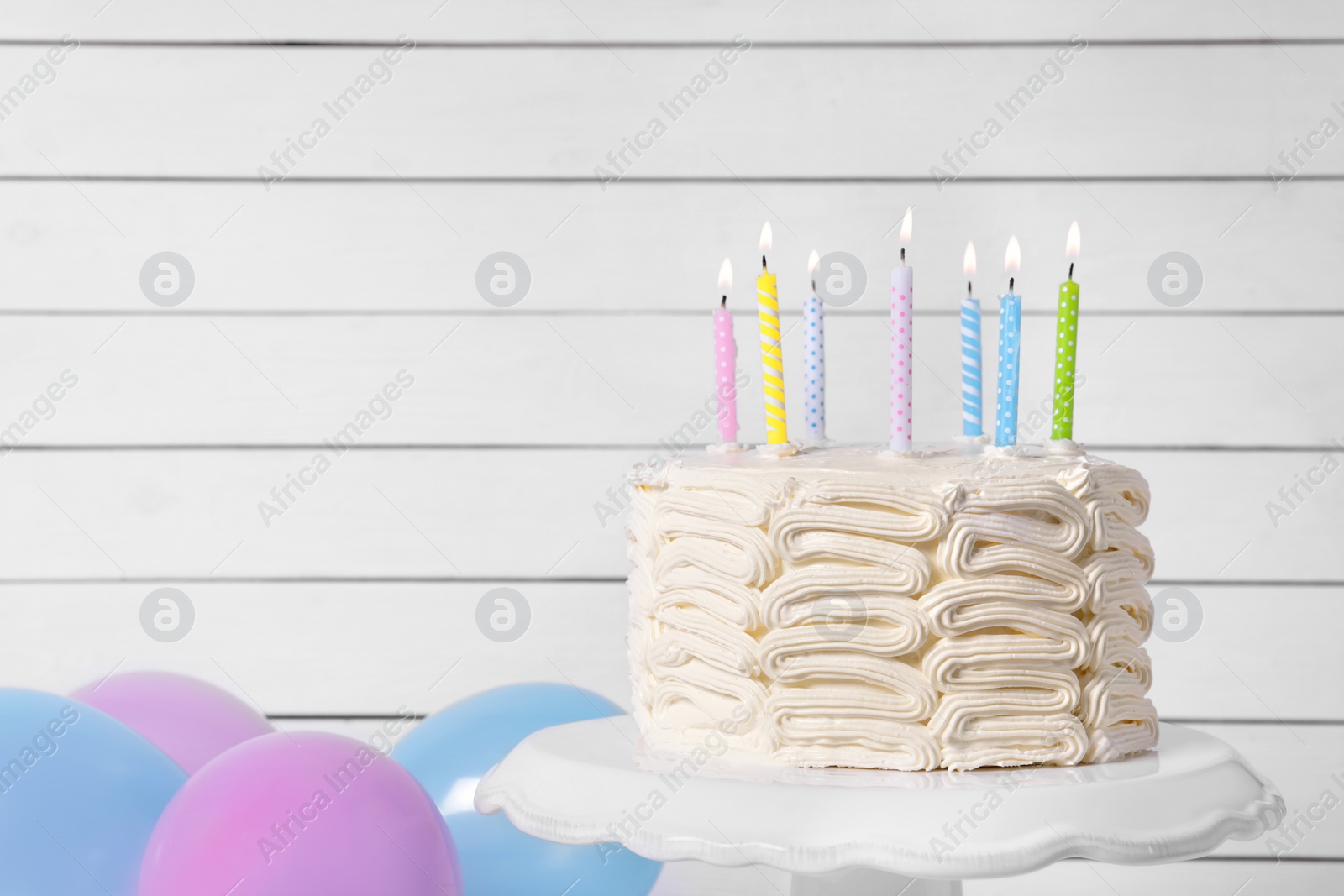 Photo of Delicious cake with burning candles and festive decor near white wall. Space for text